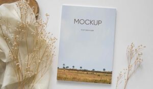 موکاپ جلد کتاب قرارداده شده کنار پارچه و گیاهان جذاب خشک زینتی